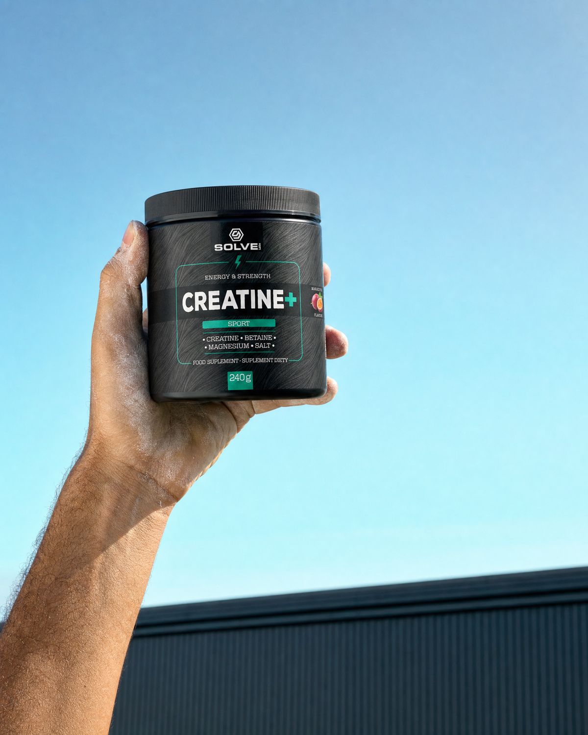A hand holding up the tub of Solve Labs Creatine+ against a clear sky