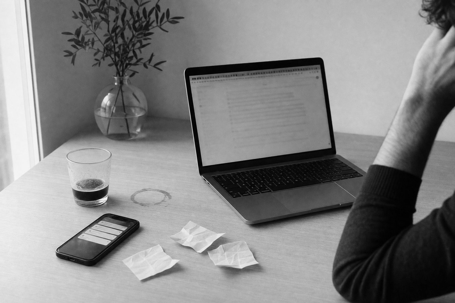 A desk at four in the afternoon: a phone lit with notifications, a cold coffee, crumpled notes, a hand at the temple