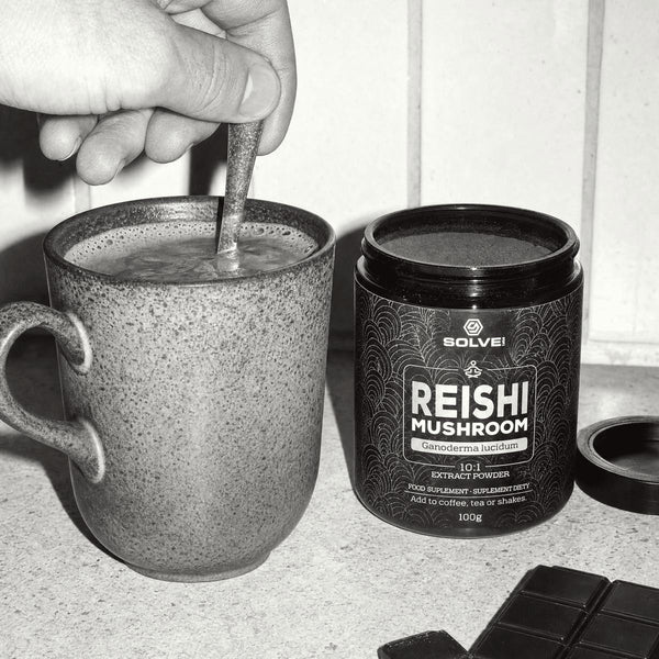 A hand stirring a mug of cacao beside a jar of Reishi