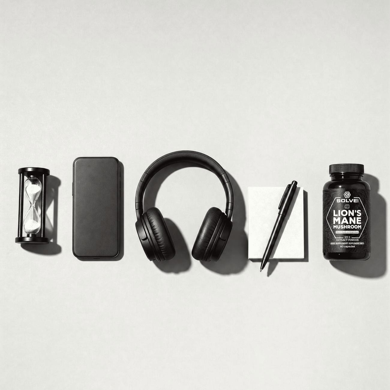 An hourglass, a phone, headphones, a notepad and a jar of Lion's Mane in a row, in black and white