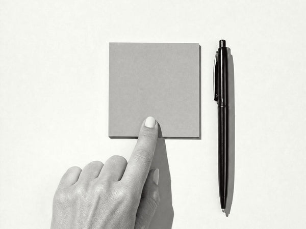 A fingertip pressing one sticky note onto a desk