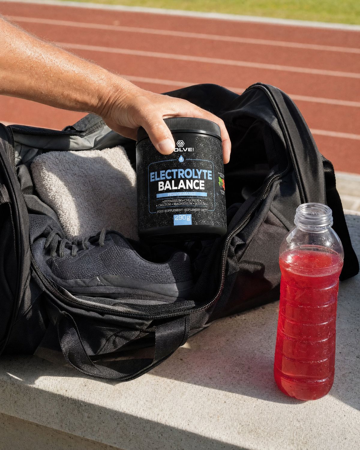 A hand lowering the tub into a sports bag beside a bottle of the red drink