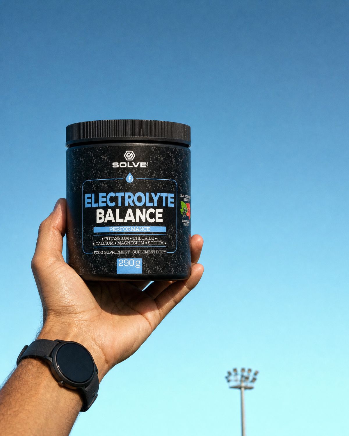 A hand holding up the tub of Solve Labs Electrolyte Balance against a clear morning sky