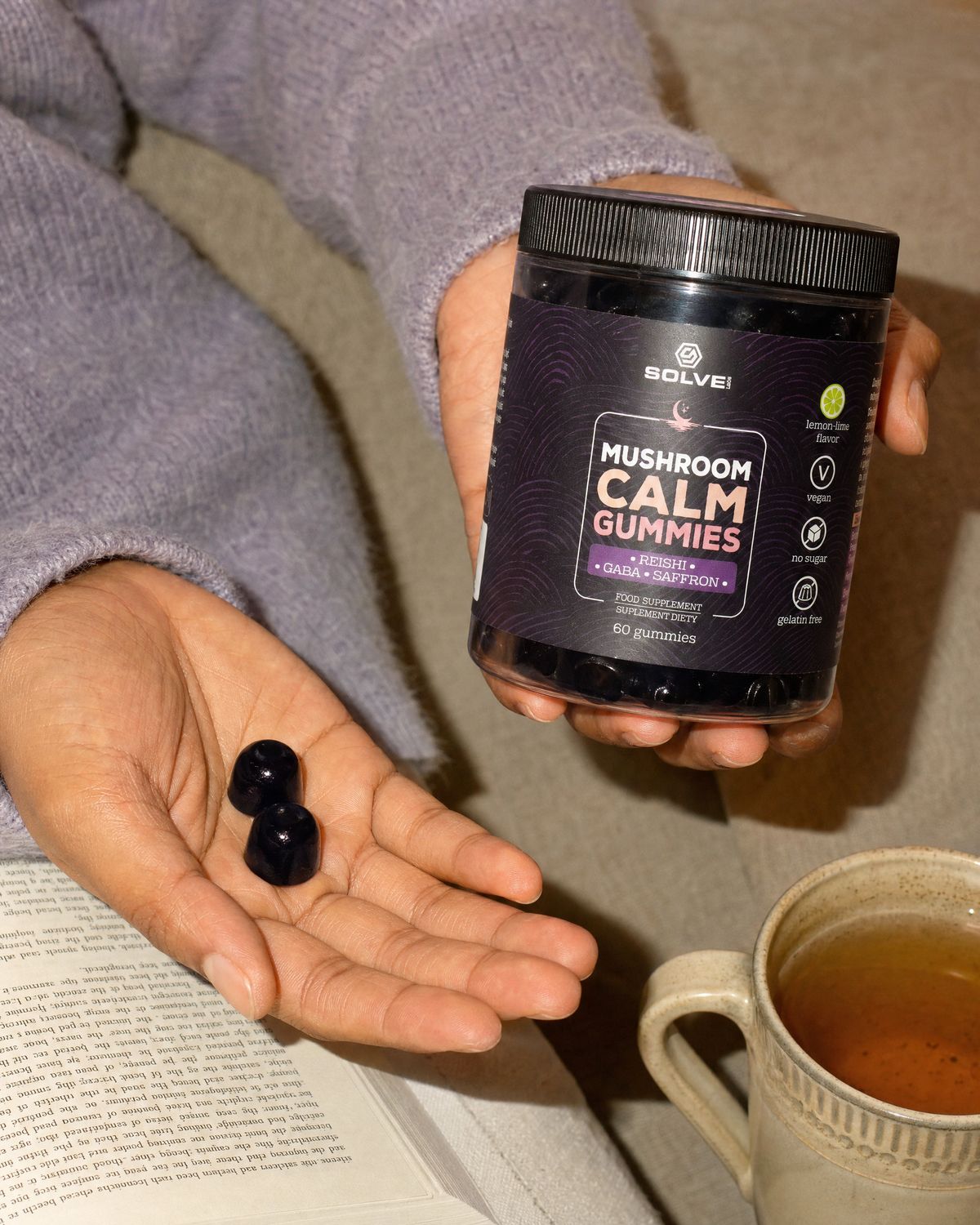 Two Calm gummies in an open palm beside the jar, a paperback and a mug of herbal tea