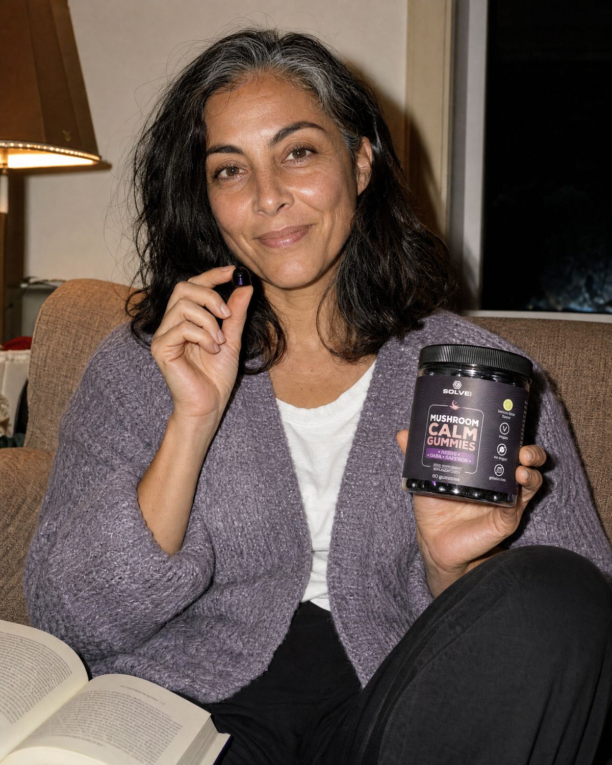 A woman on a sofa holding up a Calm gummy and the jar