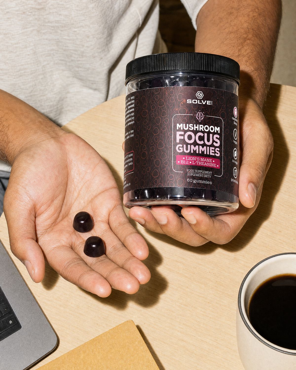 Two Focus gummies in an open palm beside the jar, a laptop and a mug of coffee