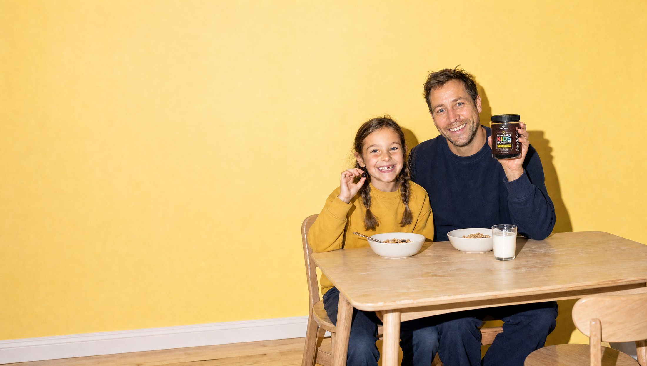 A father and his young daughter laughing at the breakfast table, the jar of Solve Labs Mushroom Kids Gummies beside their cereal bowls