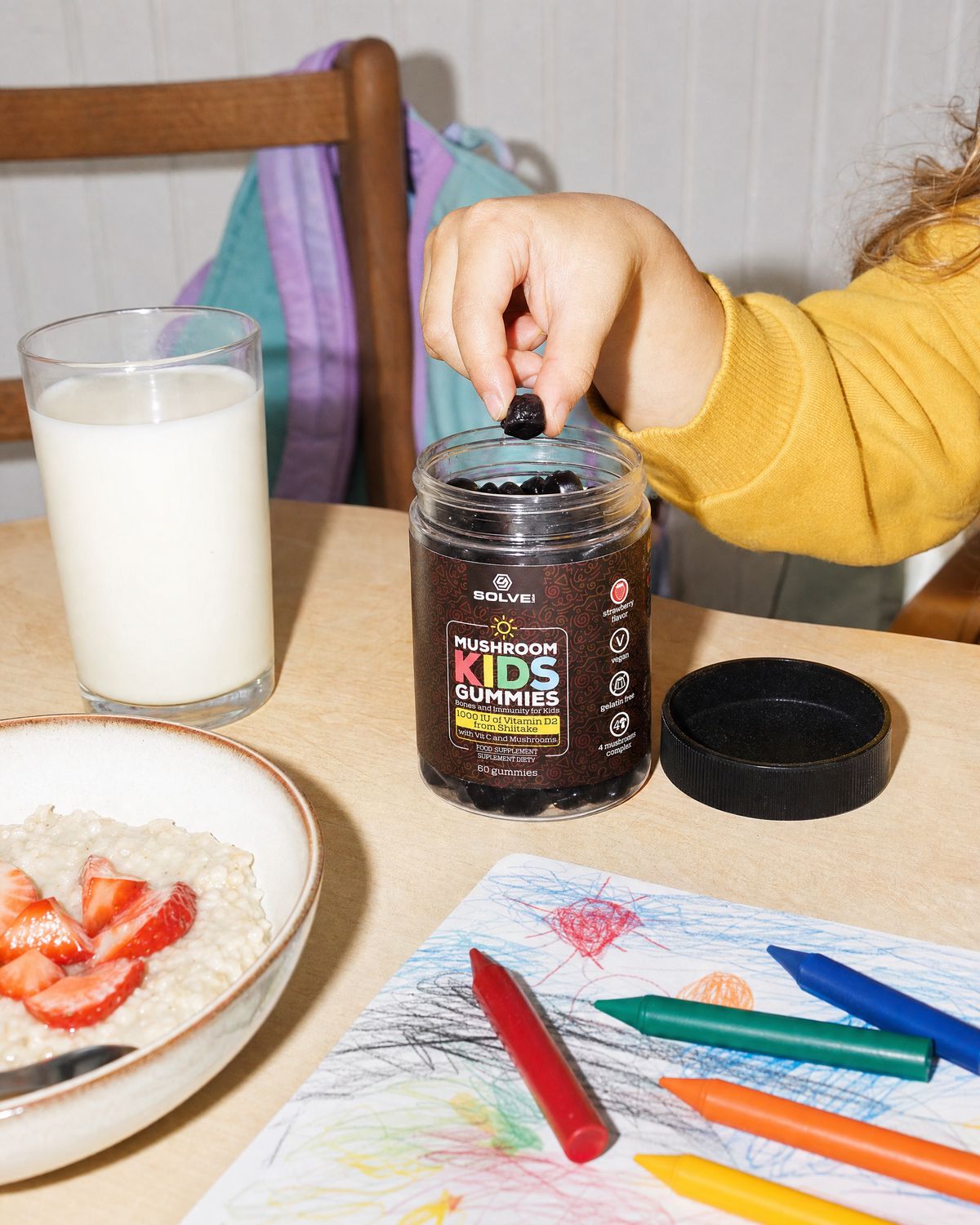 A child&rsquo;s hand lifting a gummy from the open jar on a breakfast table