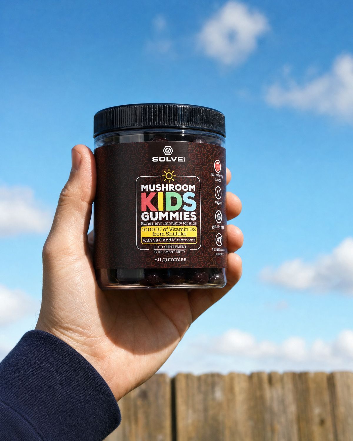 A hand holding up the jar of Solve Labs Mushroom Kids Gummies against a blue sky