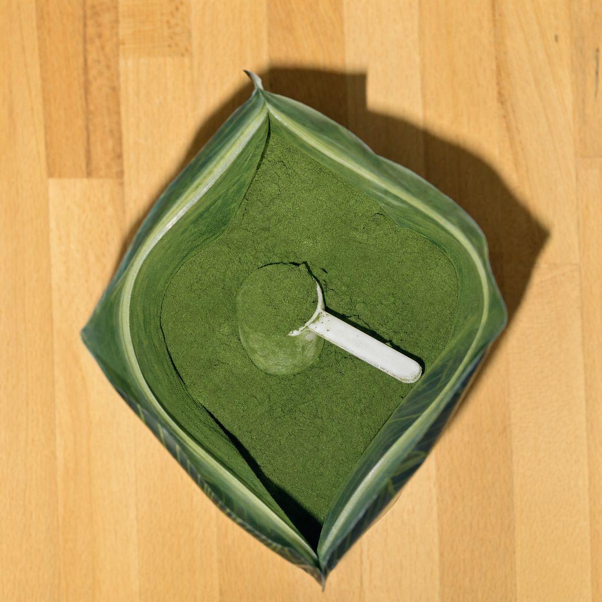 Looking into the open pouch: deep-green powder and a white scoop