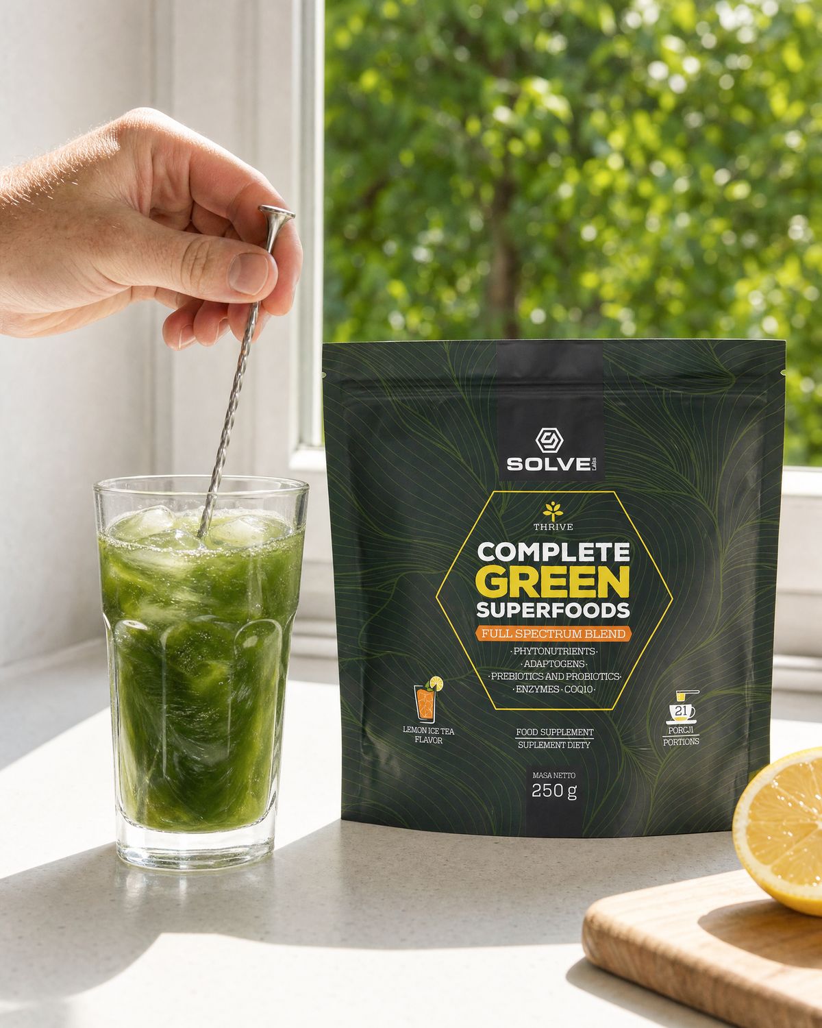 A hand stirring a tall glass of green drink with ice beside the pouch