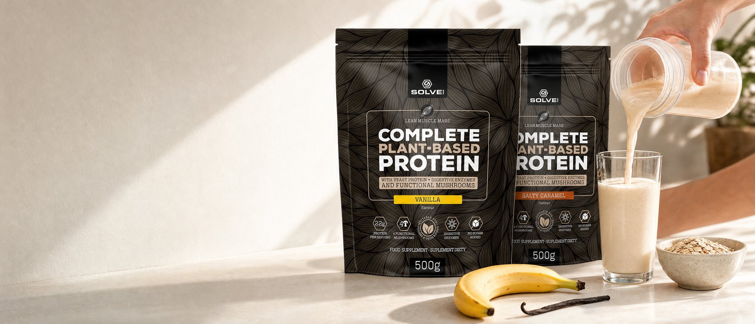 Two pouches of Solve Labs plant protein on a sunny counter, a vanilla shake being poured into a glass beside them, with a banana, oats and a vanilla pod