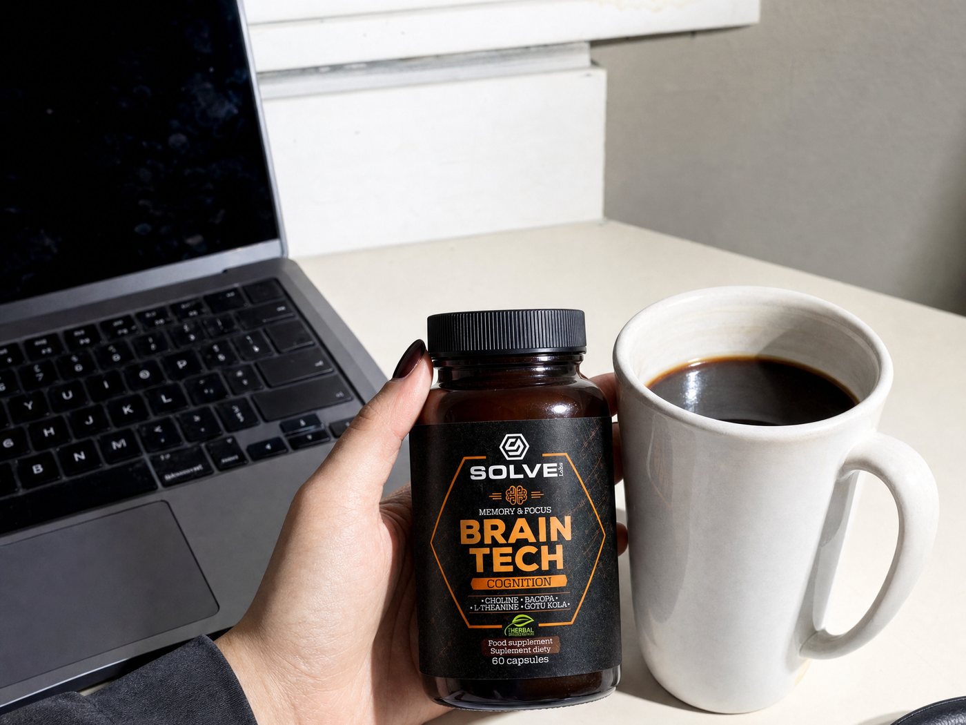 A hand holding the Brain Tech jar beside a mug of coffee on a bright desk