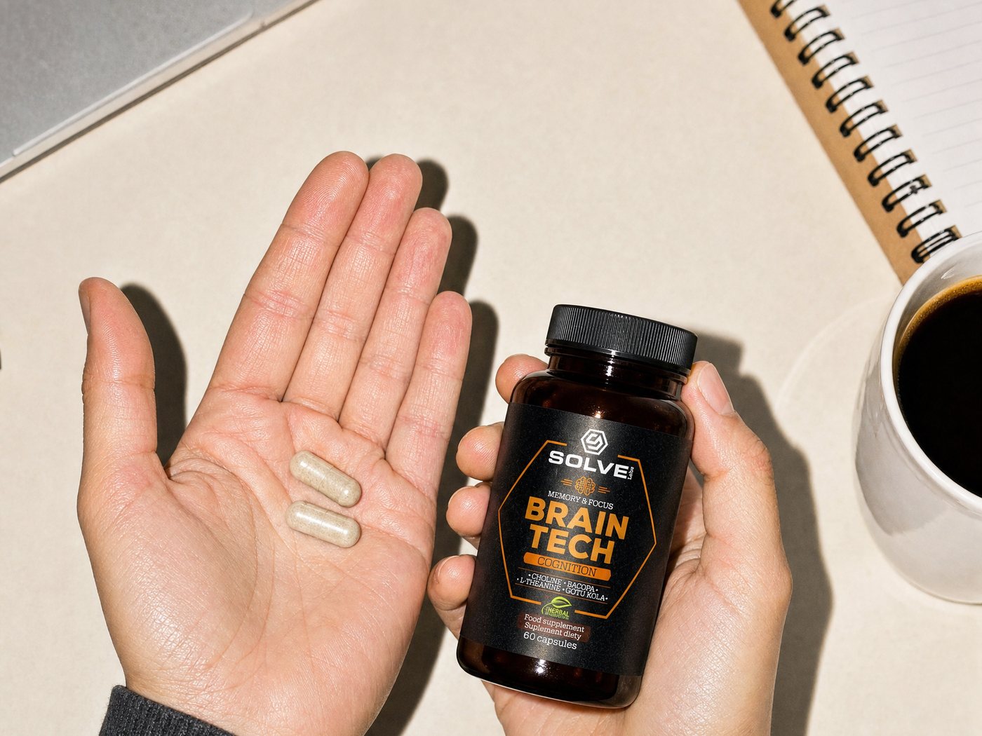 Two capsules in an open palm beside the Brain Tech jar, a cup of coffee on the desk