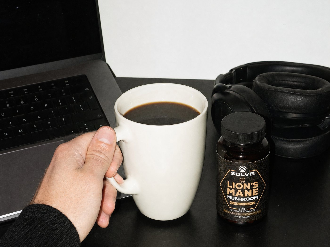 A desk seen from above: a hand on a mug of coffee, a notebook and the Lion's Mane jar