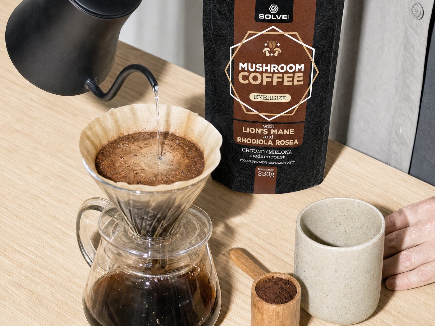 Hot water poured from a kettle over ground coffee in a pour-over, the Mushroom Coffee bag beside it