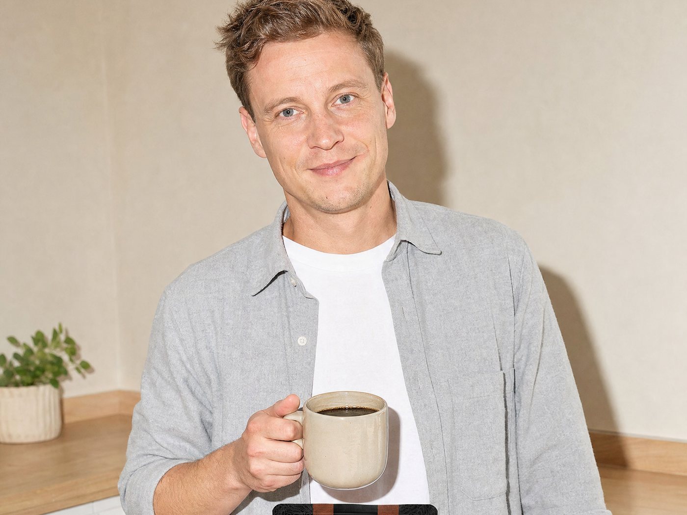A man drinking a cup of coffee in a kitchen, the Mushroom Coffee bag on the worktop in front of him