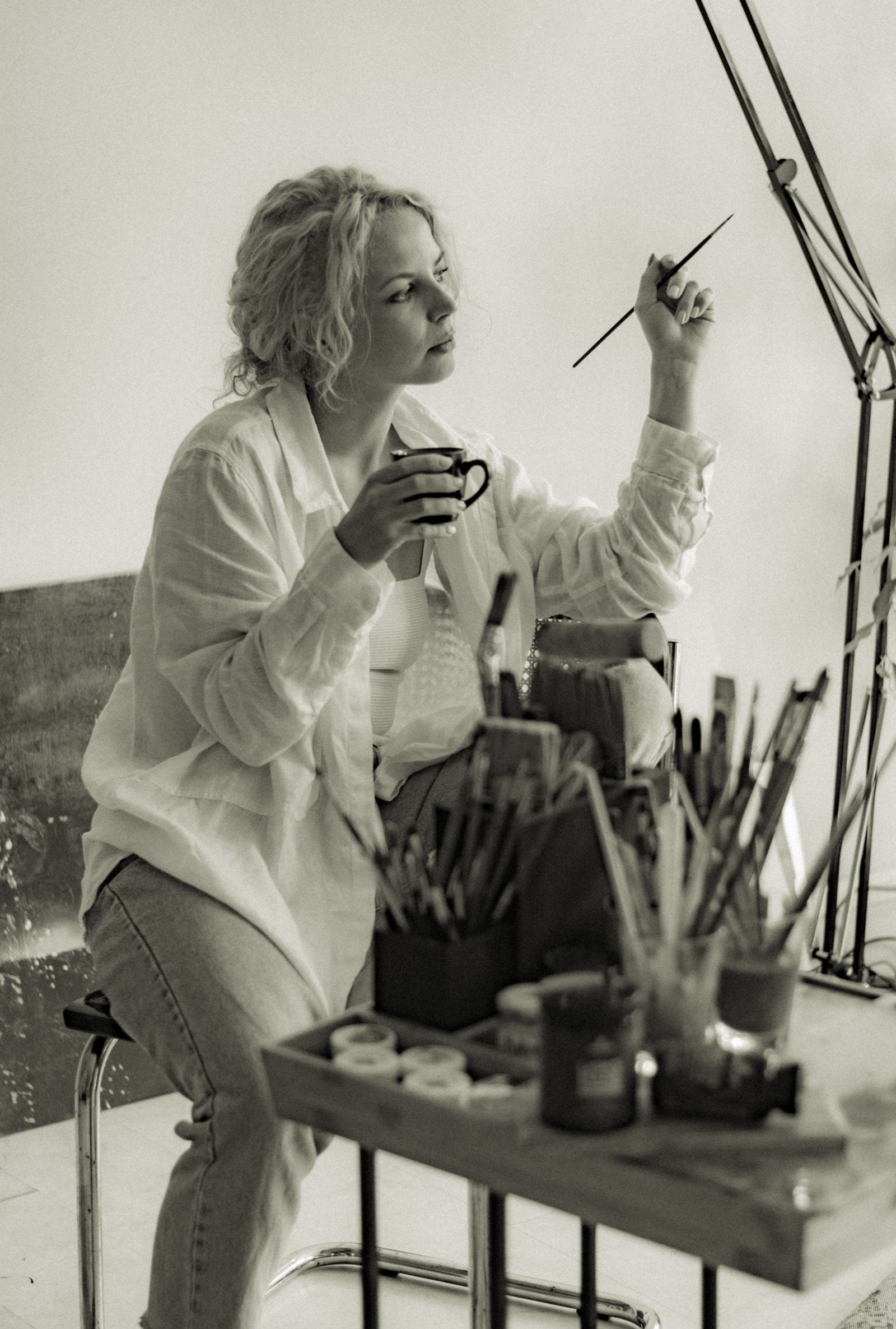 Emilia, a painter, at her brushes with a cup in one hand and a brush raised in the other