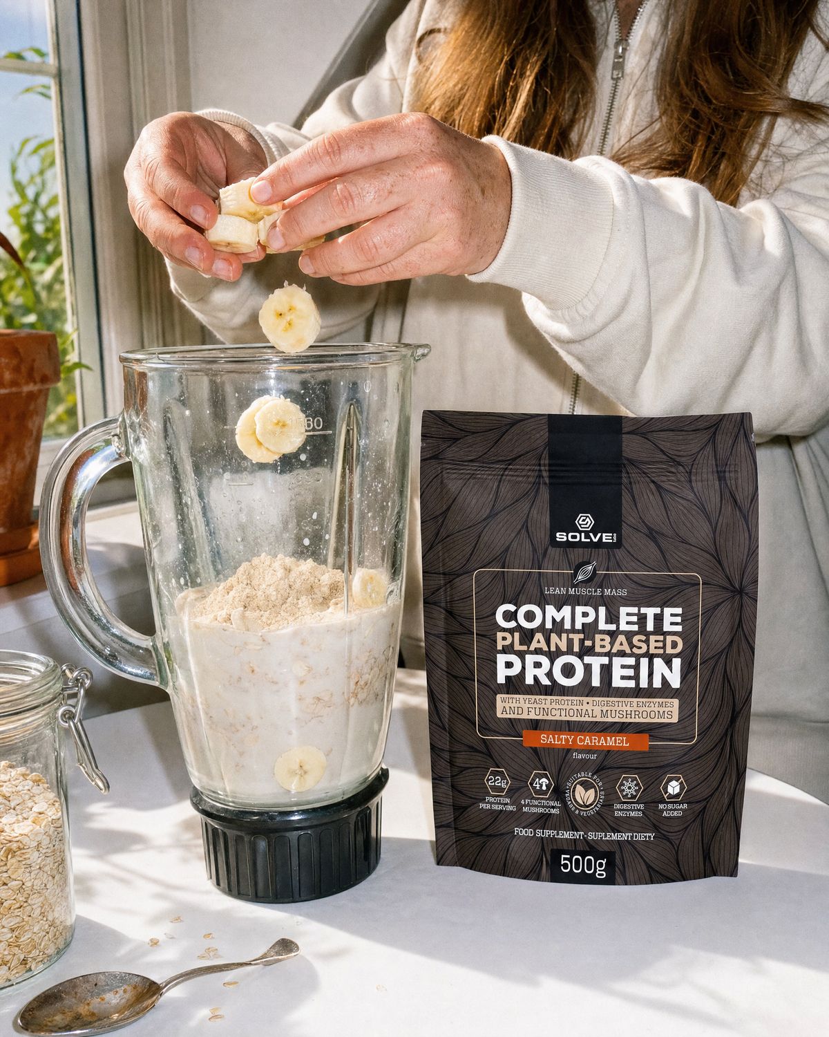Hands dropping banana into a blender beside the salted caramel pouch