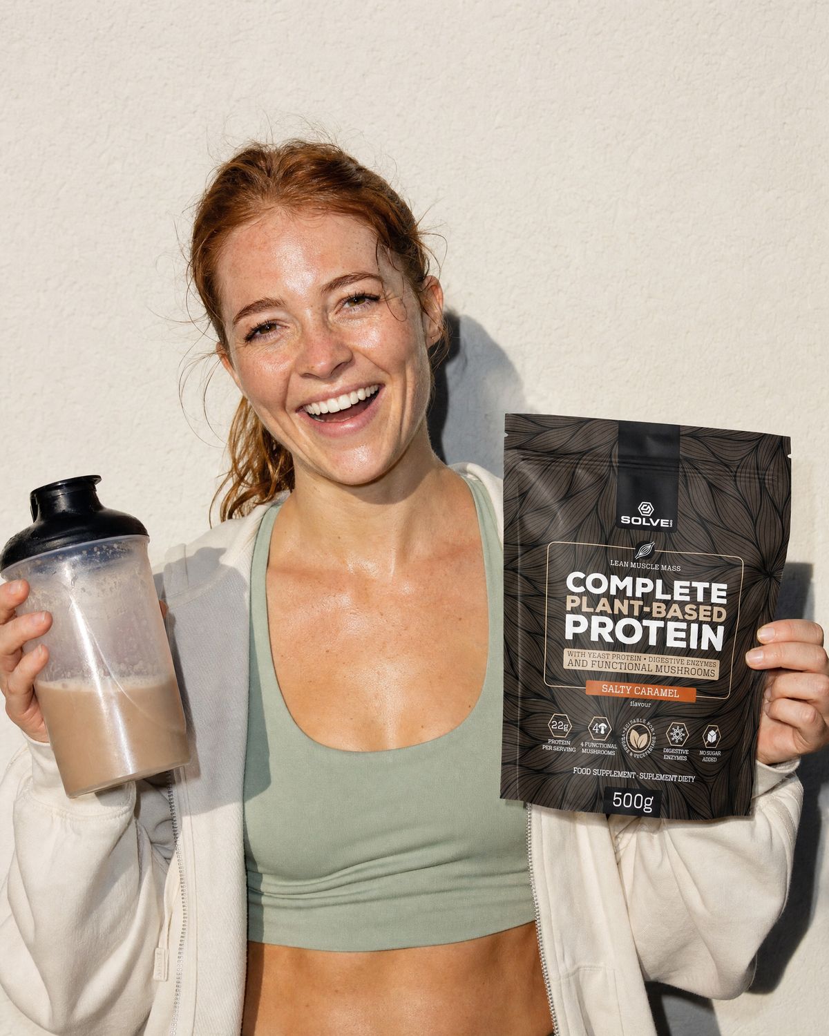 A woman laughing with a caramel shake in a shaker, holding up the salted caramel pouch