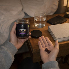 Deux Gummies Calm au Reishi dans la main, près d’une table de chevet le soir, à côté d’un verre d’eau
