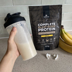 Une main qui tient un shaker de protéine végétale, le sachet derrière