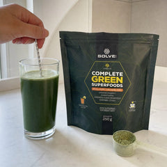 Une main qui remue un verre de Superaliments verts, le sachet à côté