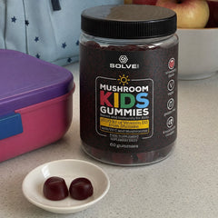 Le pot de Gummies pour enfants sur un plan de travail de cuisine, à côté d’une boîte à goûter, d’un sac à dos et d’un bol de pommes