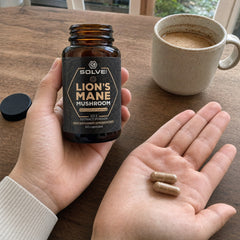 Deux gélules de Lion’s Mane dans une paume ouverte à la table du petit-déjeuner, le pot dans l’autre main