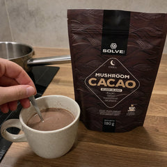 Une main qui remue une tasse de Cacao aux champignons le soir, le sachet à côté