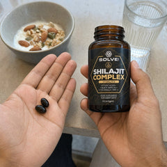 Deux capsules molles de Complexe de shilajit dans une paume ouverte à la table du petit-déjeuner, le pot dans l’autre main