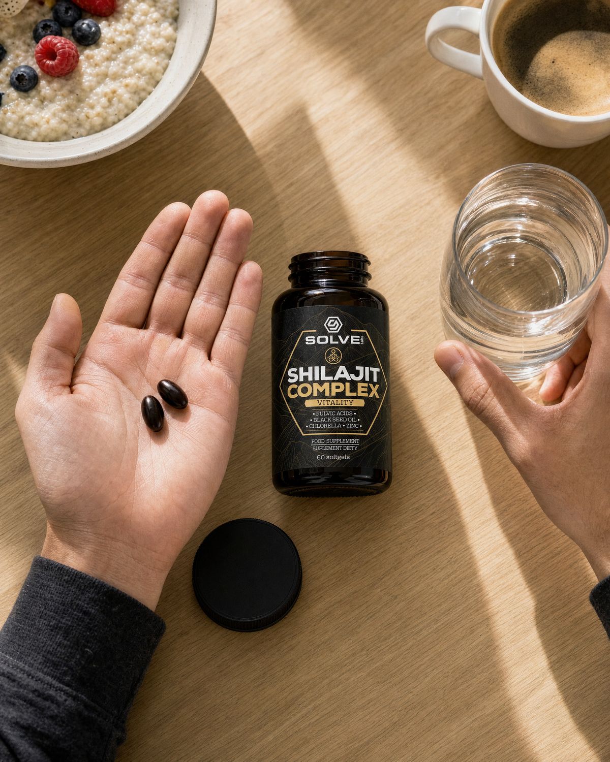 Two dark softgels in an open palm on an oak table beside a glass of water and the open jar