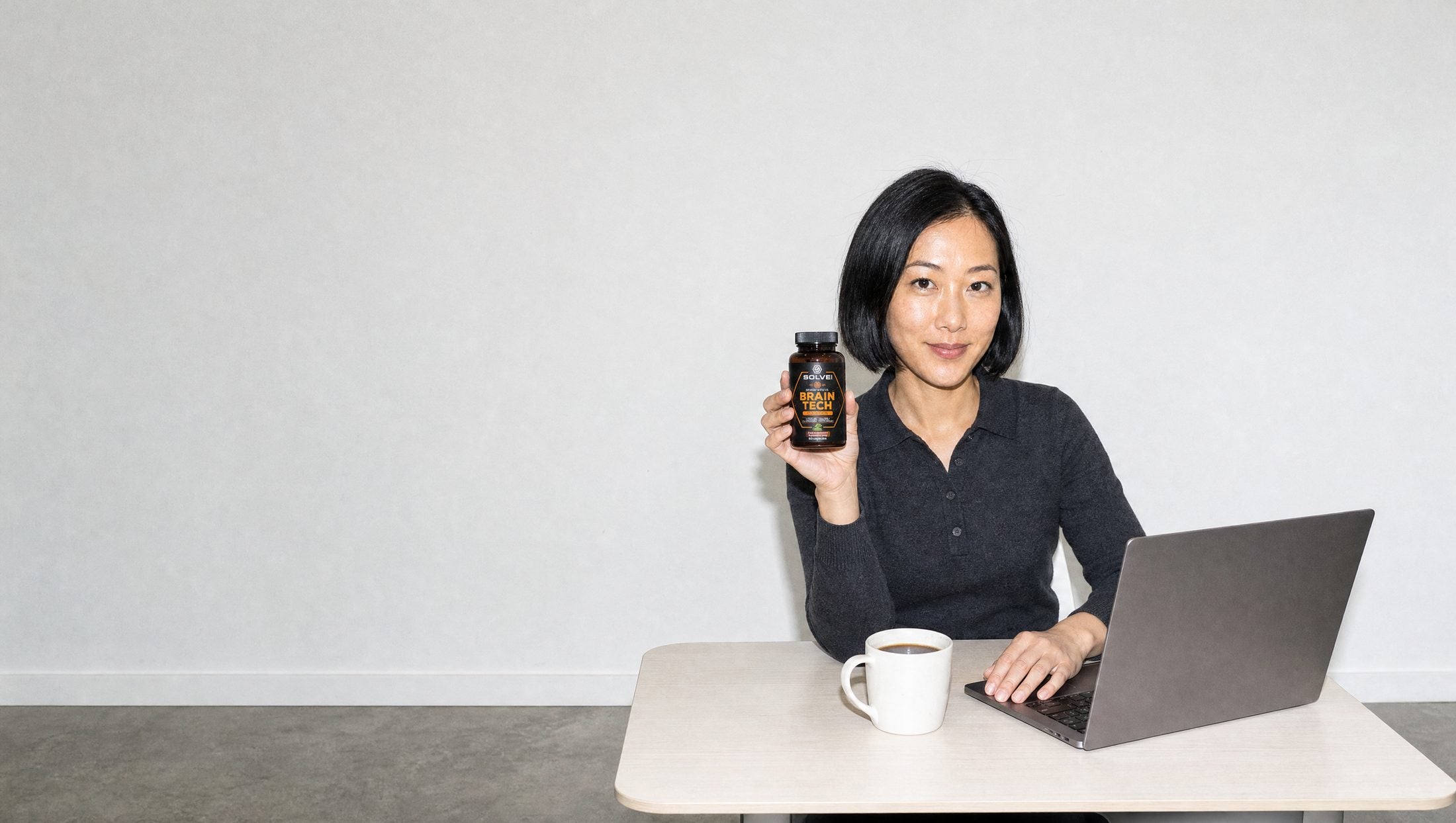 A woman at her desk with a laptop and a coffee, holding a jar of Solve Labs Brain Tech