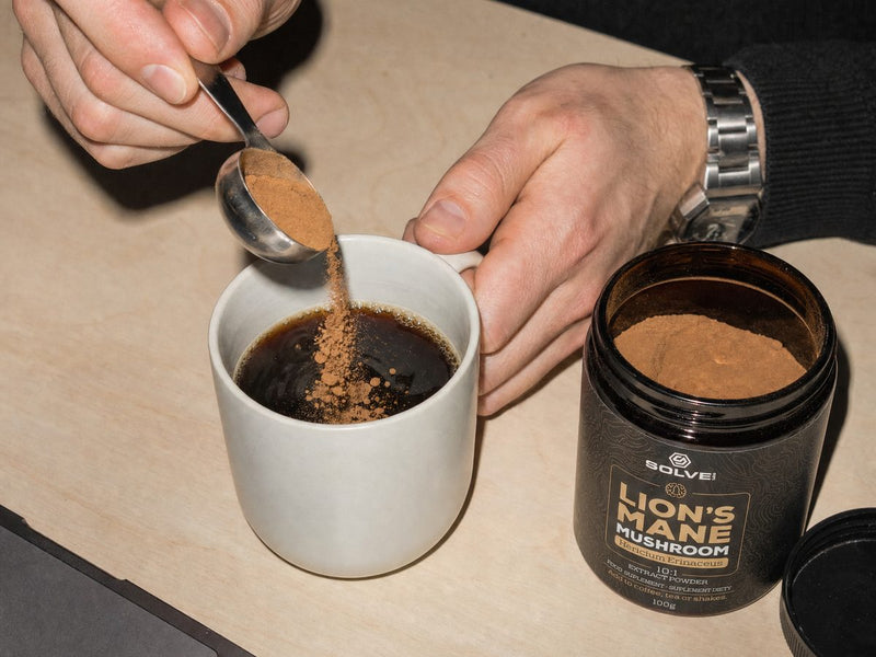 A spoon of Lion&rsquo;s Mane powder going into a mug of black coffee