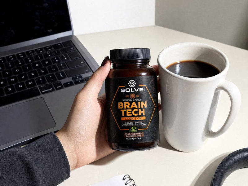 A hand holding a jar of Brain Tech beside a laptop and a mug of coffee