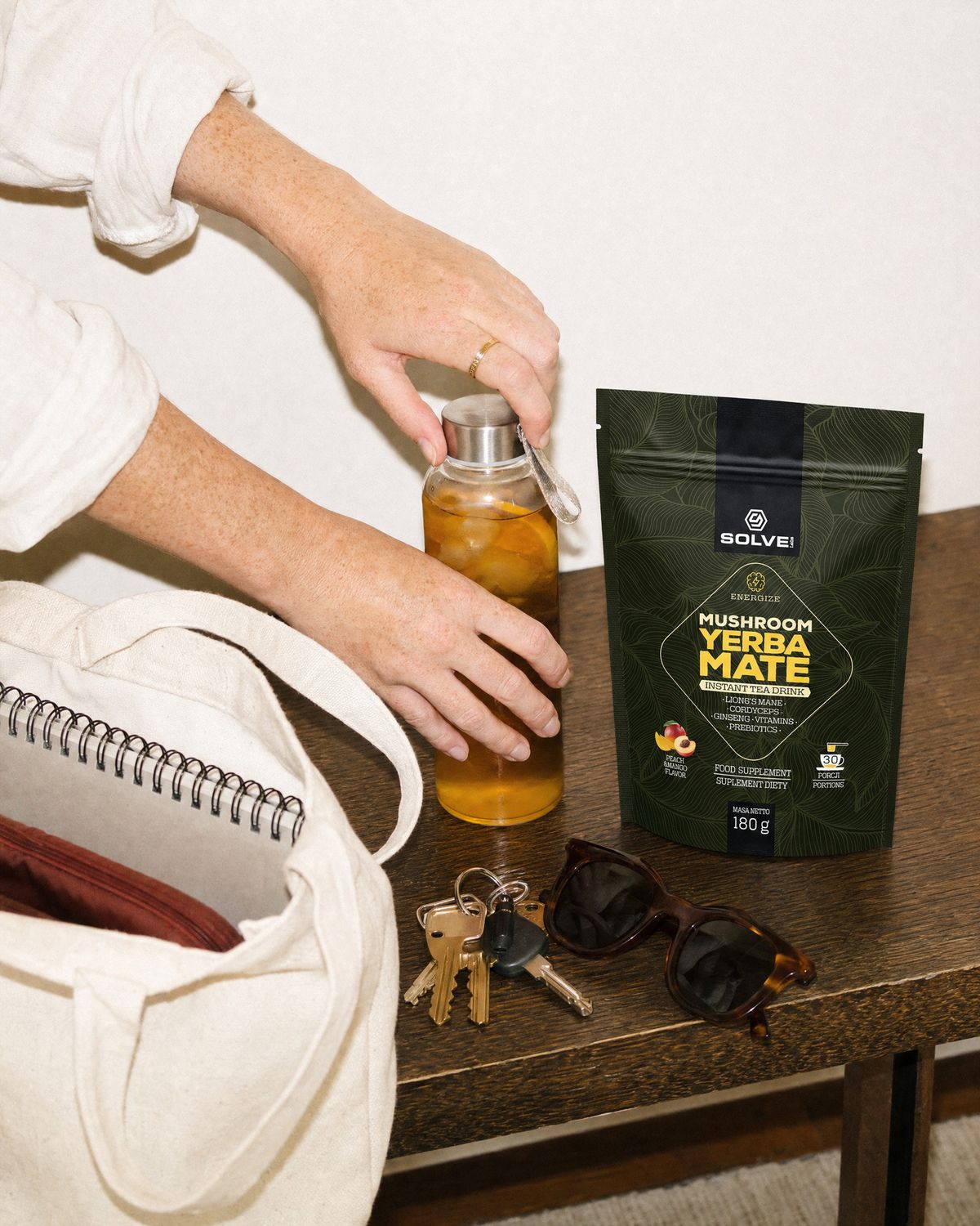 Hands closing a bottle of iced yerba mate beside a tote bag and the pouch