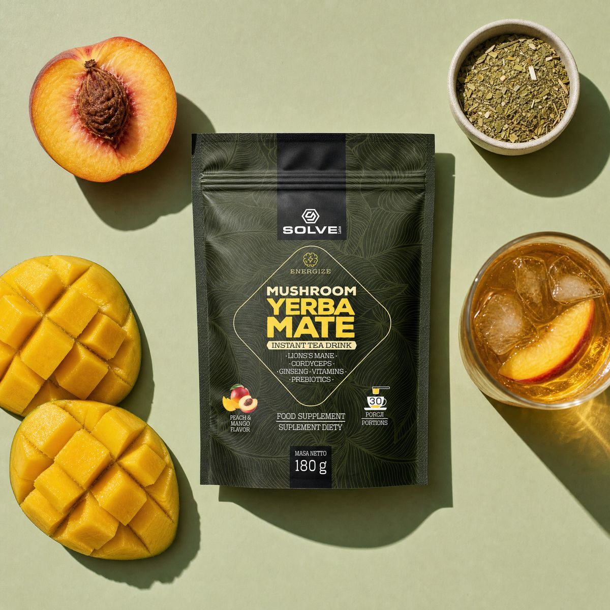 The pouch of Solve Labs Mushroom Yerba Mate from above with a halved peach, mango cheeks, dried yerba mate leaves and a glass of the drink
